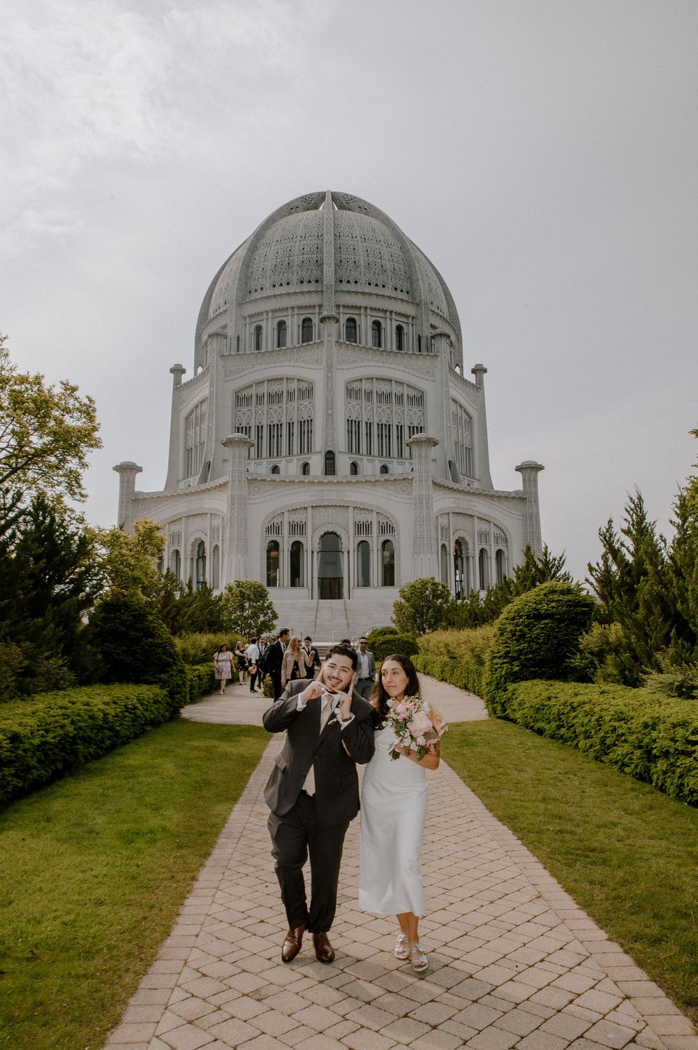 A grand Baha'i House of Worship with its iconic domed structure rises behind a paved path lined with manicured gardens.