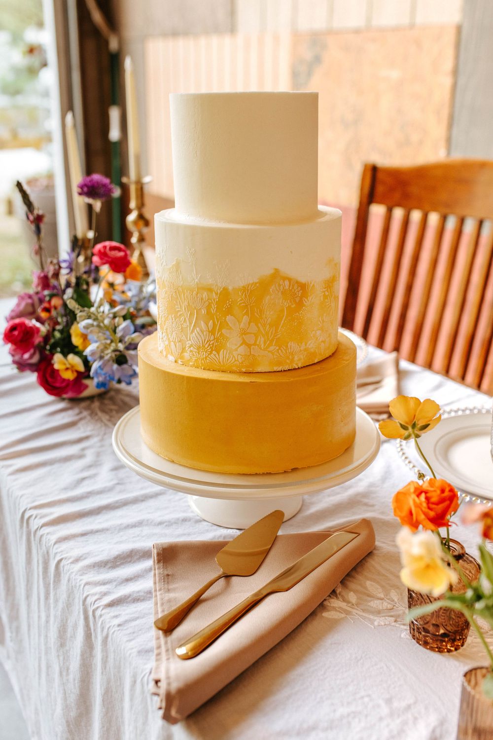 Four sequential shots of a yellow and white wedding cake with serving utensils on a white tablecloth with colorful flowers.