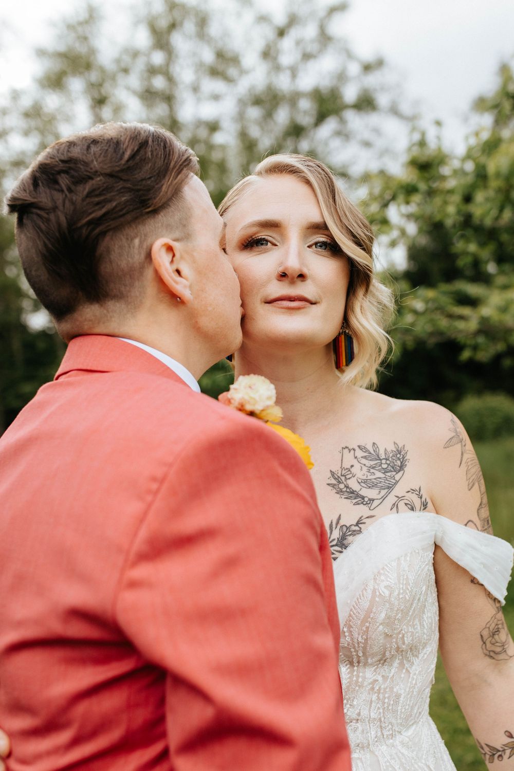 Romantic wedding couple embracing outdoors, with bride wearing white lace dress and visible floral tattoos.