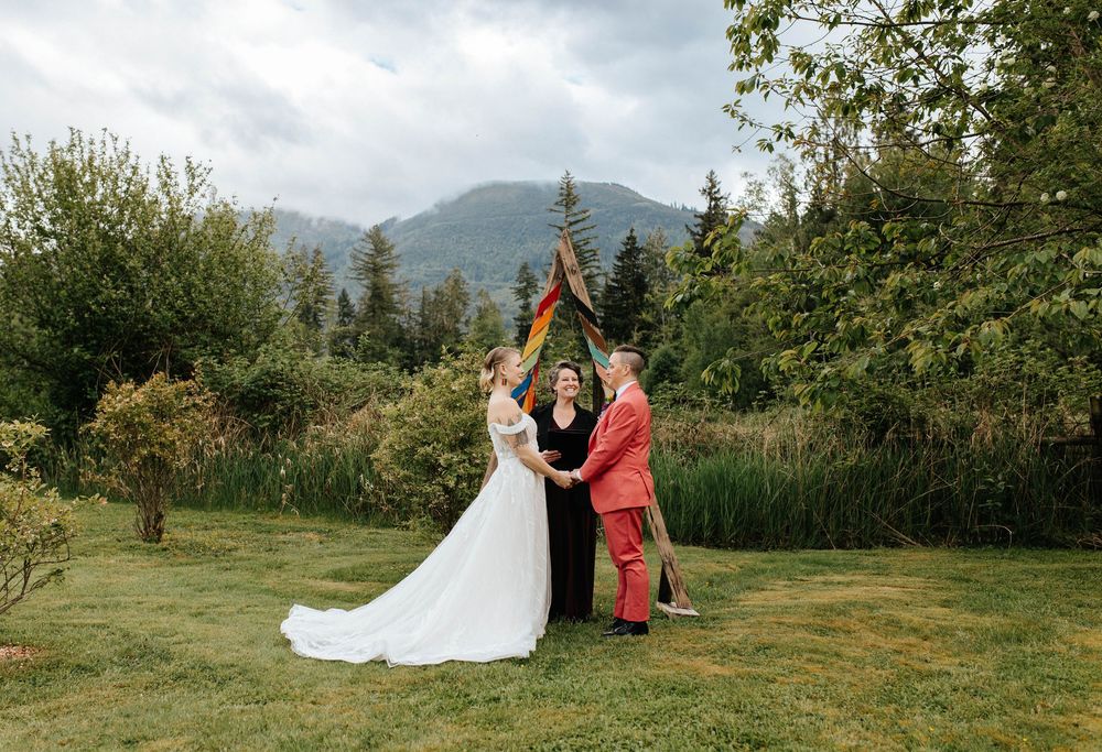 An outdoor wedding ceremony takes place in a lush garden setting with mountains visible in the misty backdrop.