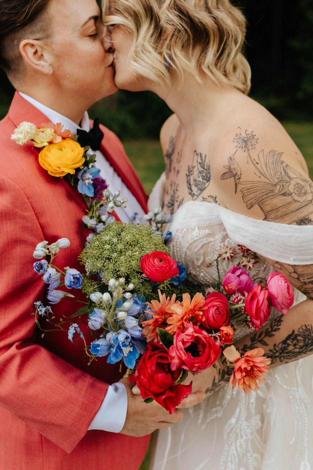 A romantic wedding moment featuring vibrant red and blue florals with the bride showing intricate arm tattoos.