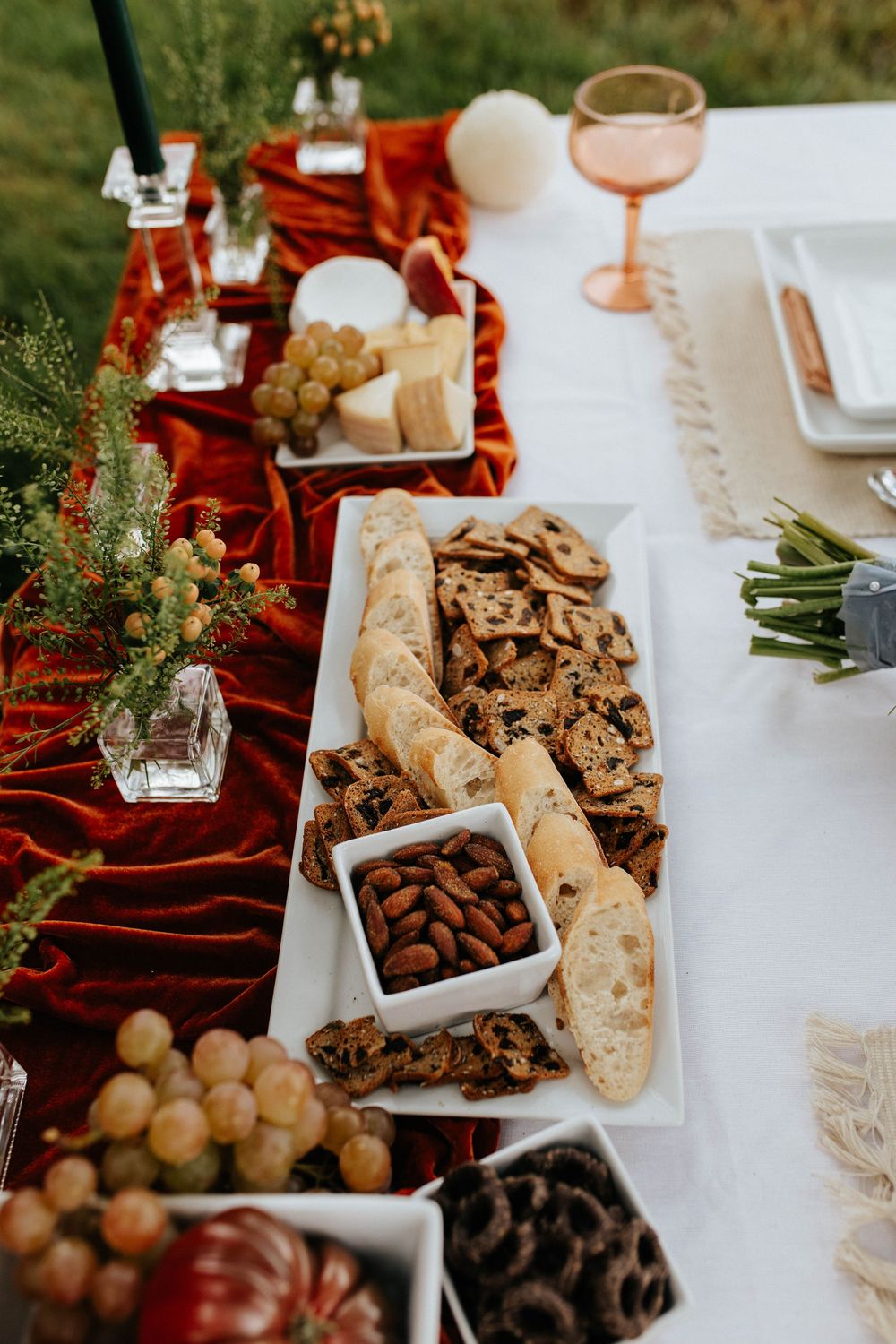 Festive holiday table setting with charcuterie board featuring bread, almonds, grapes and greenery on red velvet runner.