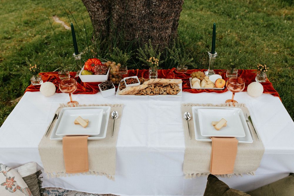 Elegant outdoor table setting with white linens, peach napkins and fall decor beneath a large tree.