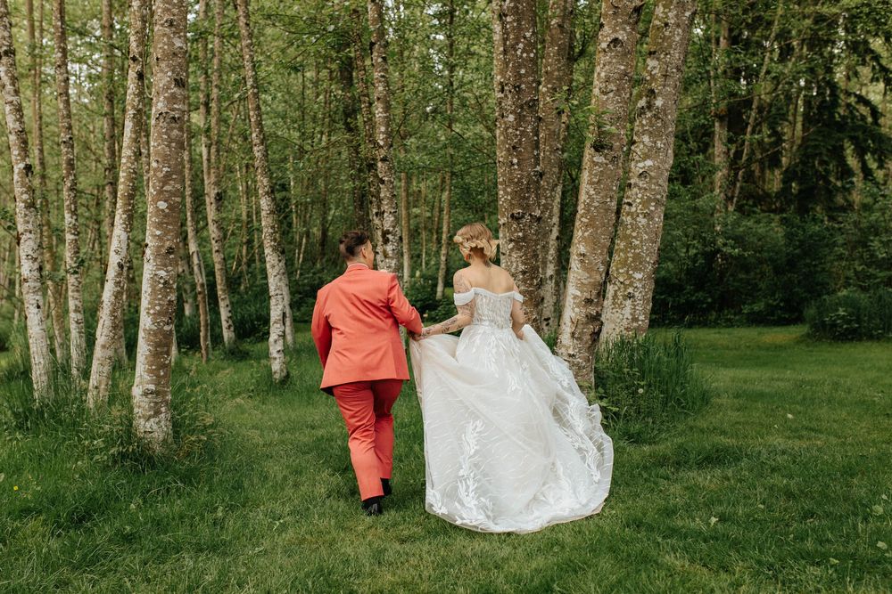 Two people walk together through a scenic birch forest grove on a grassy path in wedding attire.