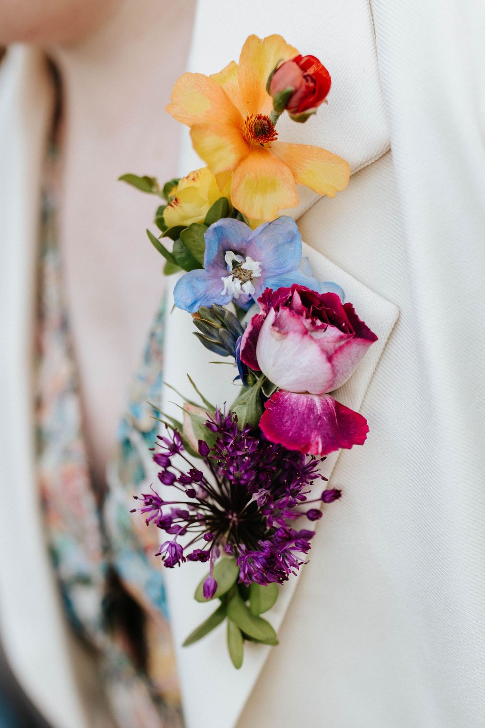 Delicate boutonniere featuring purple cornflower, yellow daffodil, and pink peony flowers against a light background.
