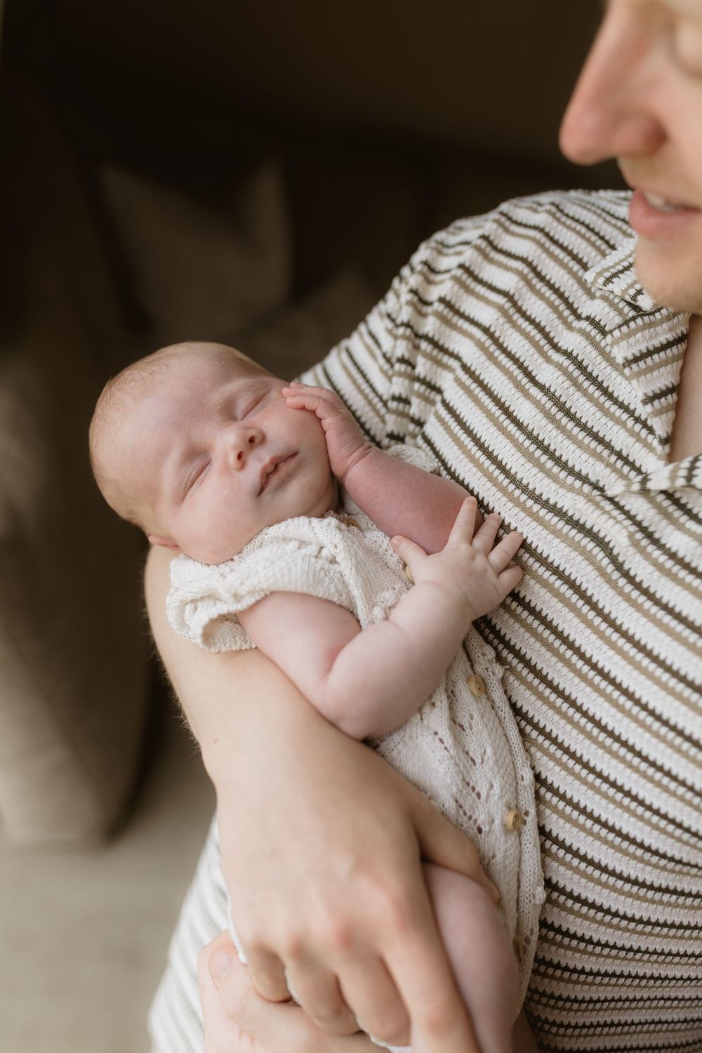 A sleeping newborn baby in white lace clothing rests peacefully against a caregiver's striped shirt.