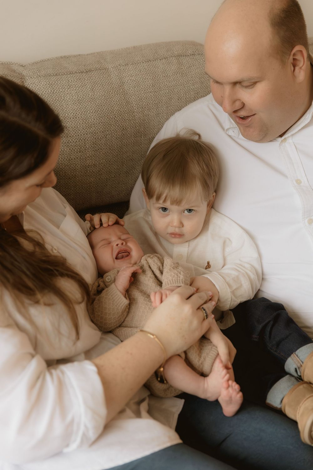Family sitting together on couch sharing intimate moment with young toddler in casual clothing.
