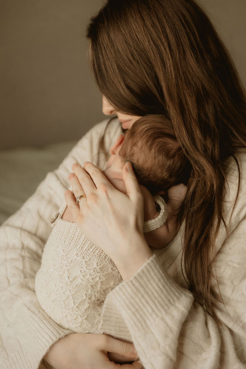 A tender moment captured as someone wearing a cream sweater cradles and embraces a baby against their shoulder.