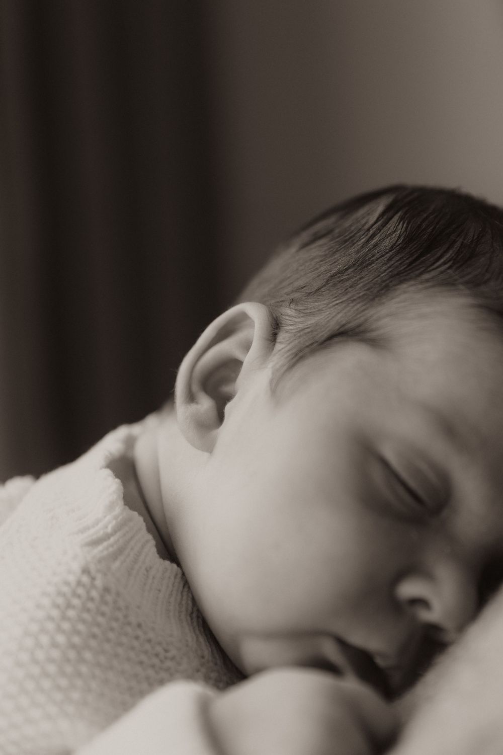Close-up sepia portrait of a peaceful sleeping baby in a knit sweater.