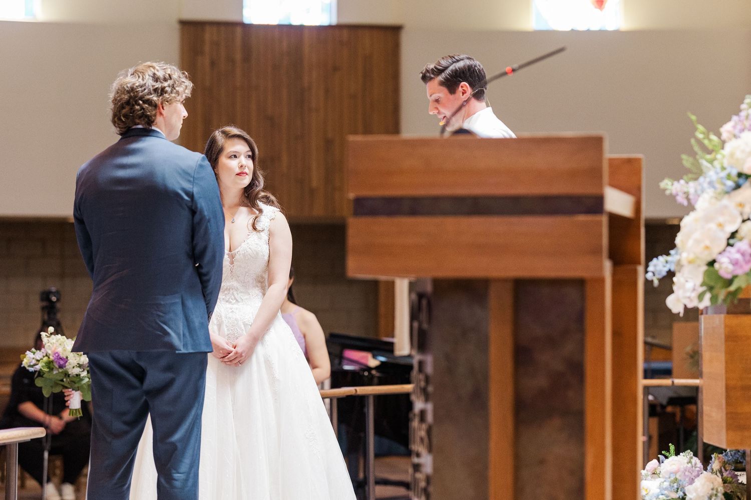 A traditional wedding ceremony takes place in a church sanctuary with wood paneling and floral decorations.