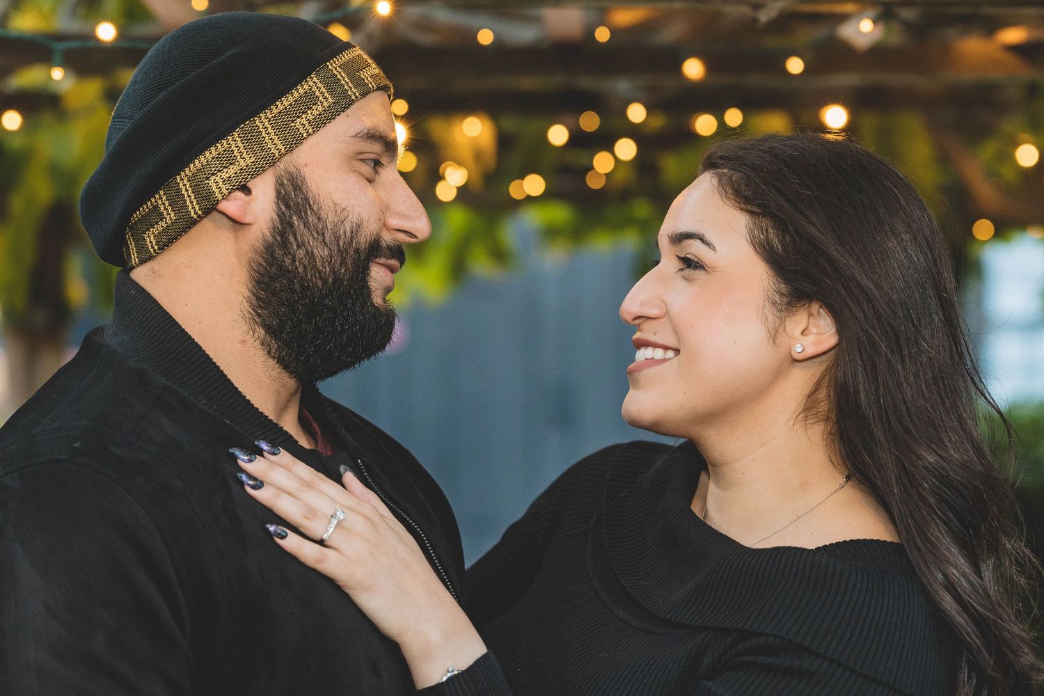 A couple shares a joyful moment together with twinkling lights in the background during an engagement photoshoot.