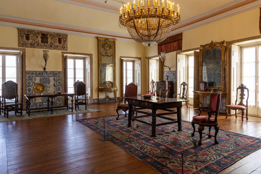 Panoramic view of an elegant palace room with ornate chandeliers, polished wooden floors and decorative rugs.