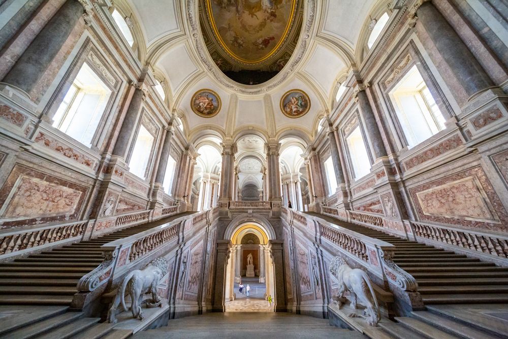 Ornate baroque marble staircase with symmetrical dual staircases and painted ceilings in an elegant palace interior.