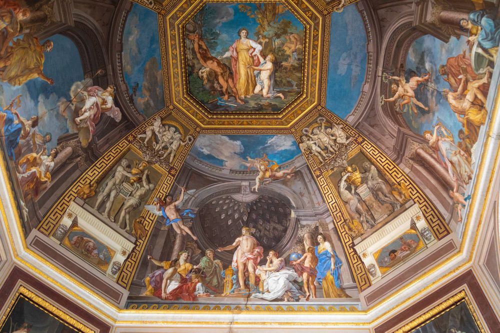 Ornate Renaissance ceiling fresco depicting religious and mythological scenes in vibrant colors within Vatican Museum architecture.