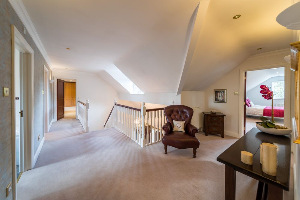 Bright upstairs hallway with plush carpeting features a leather armchair and wooden banister rail in a modern home interior.