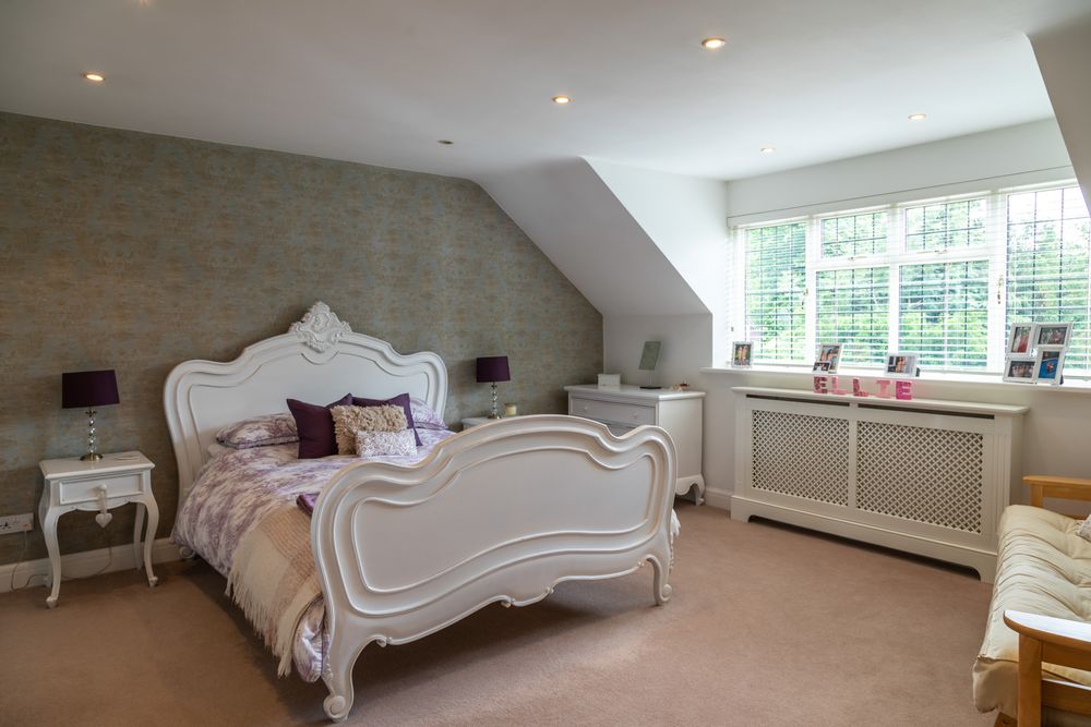 Elegant master bedroom with ornate white French-style bed frame, gray walls, and large windows in attic conversion.