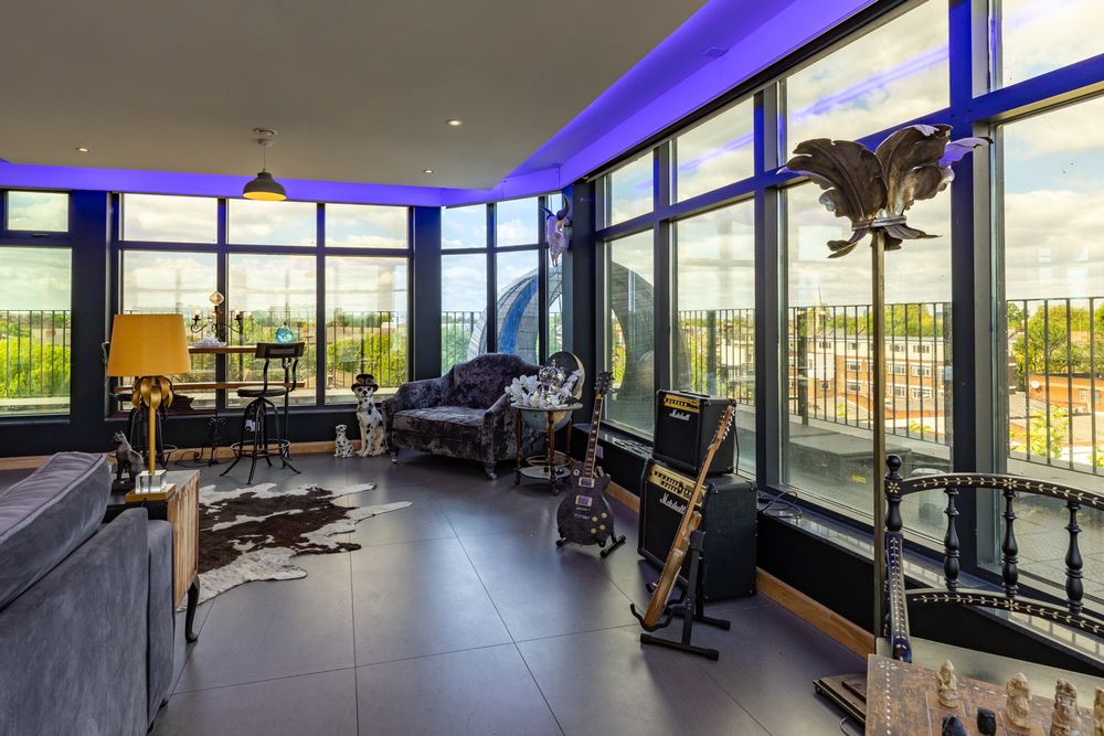 Modern penthouse living room with floor-to-ceiling windows, blue LED lighting, and contemporary black furniture.