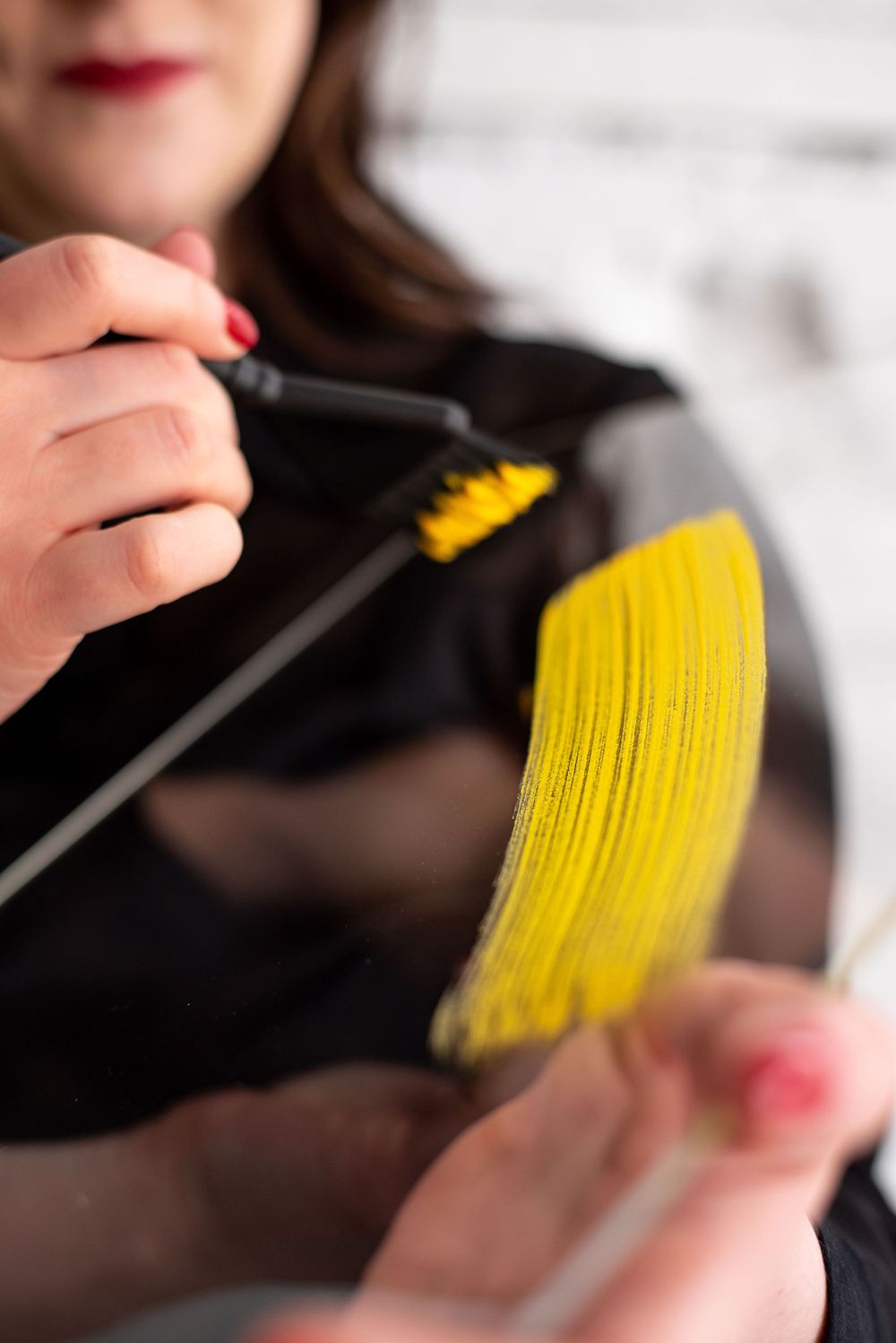 Close-up view of hands holding hair strands while brushing vibrant yellow hair dye through dark hair.