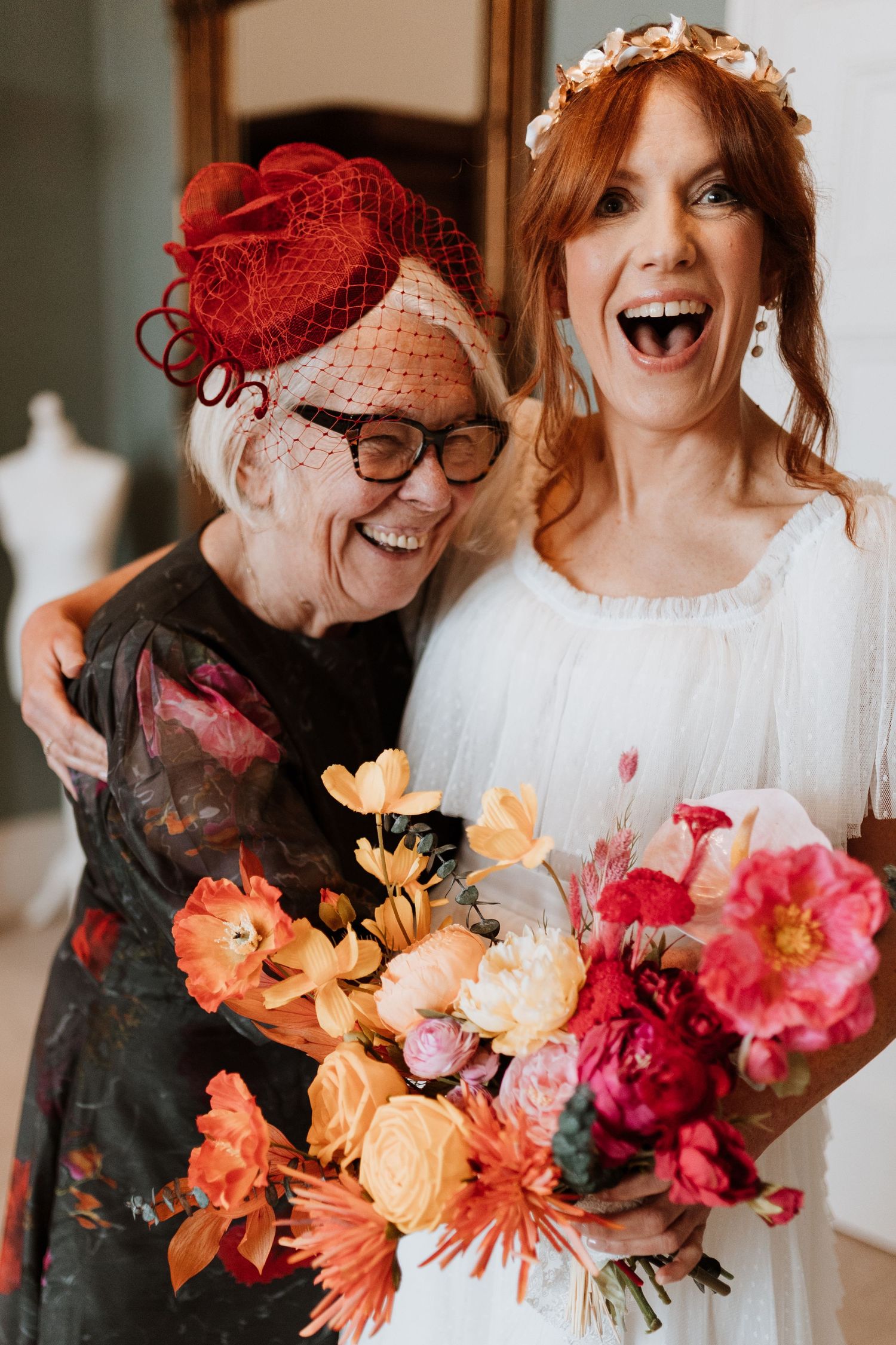 Bride and her mother share a joyful laugh while holding a vibrant orange and red flower bouquet at a formal event at Berwick House.