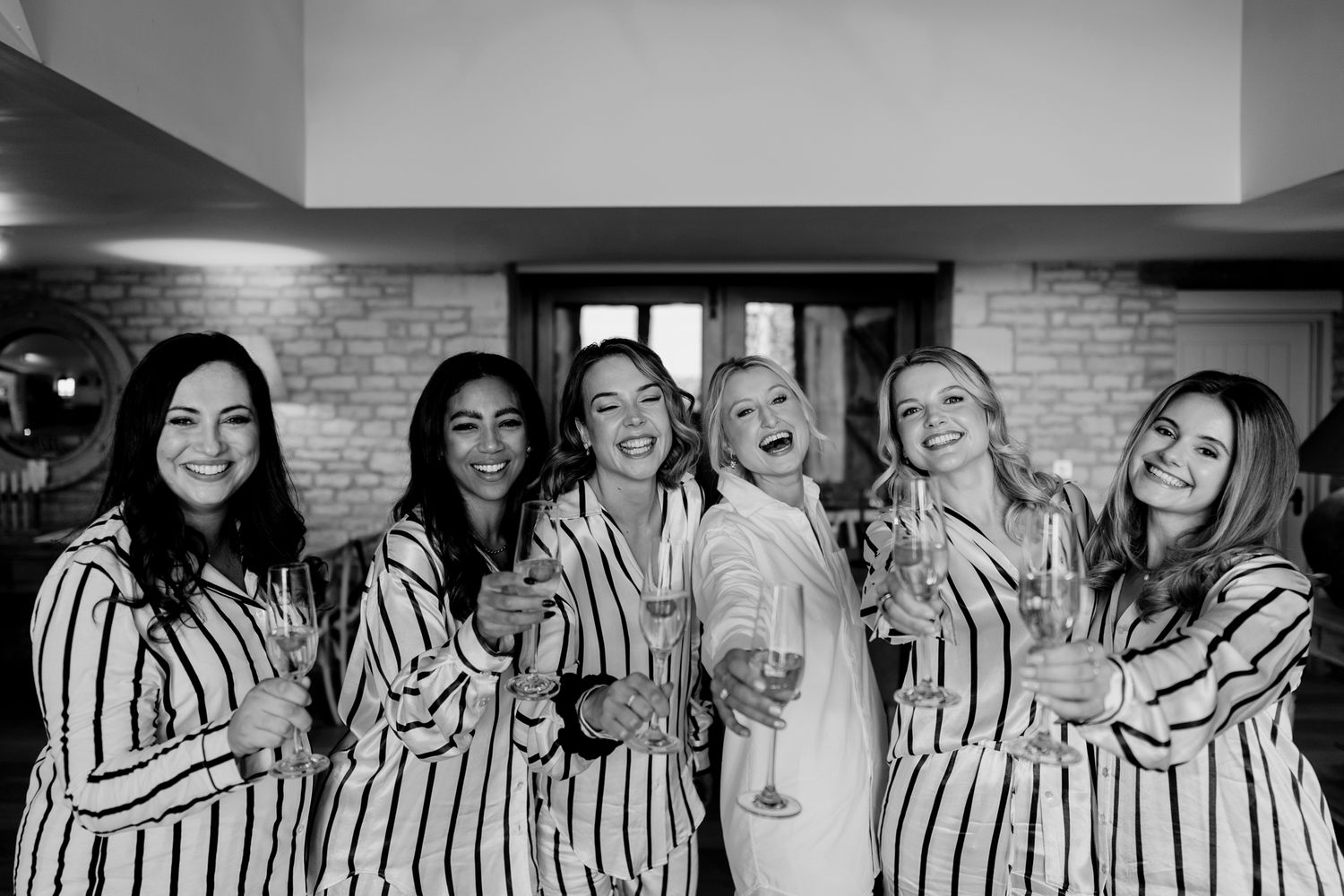 Black and white photo of a wedding party in matching striped robes holding champagne glasses and laughing together.