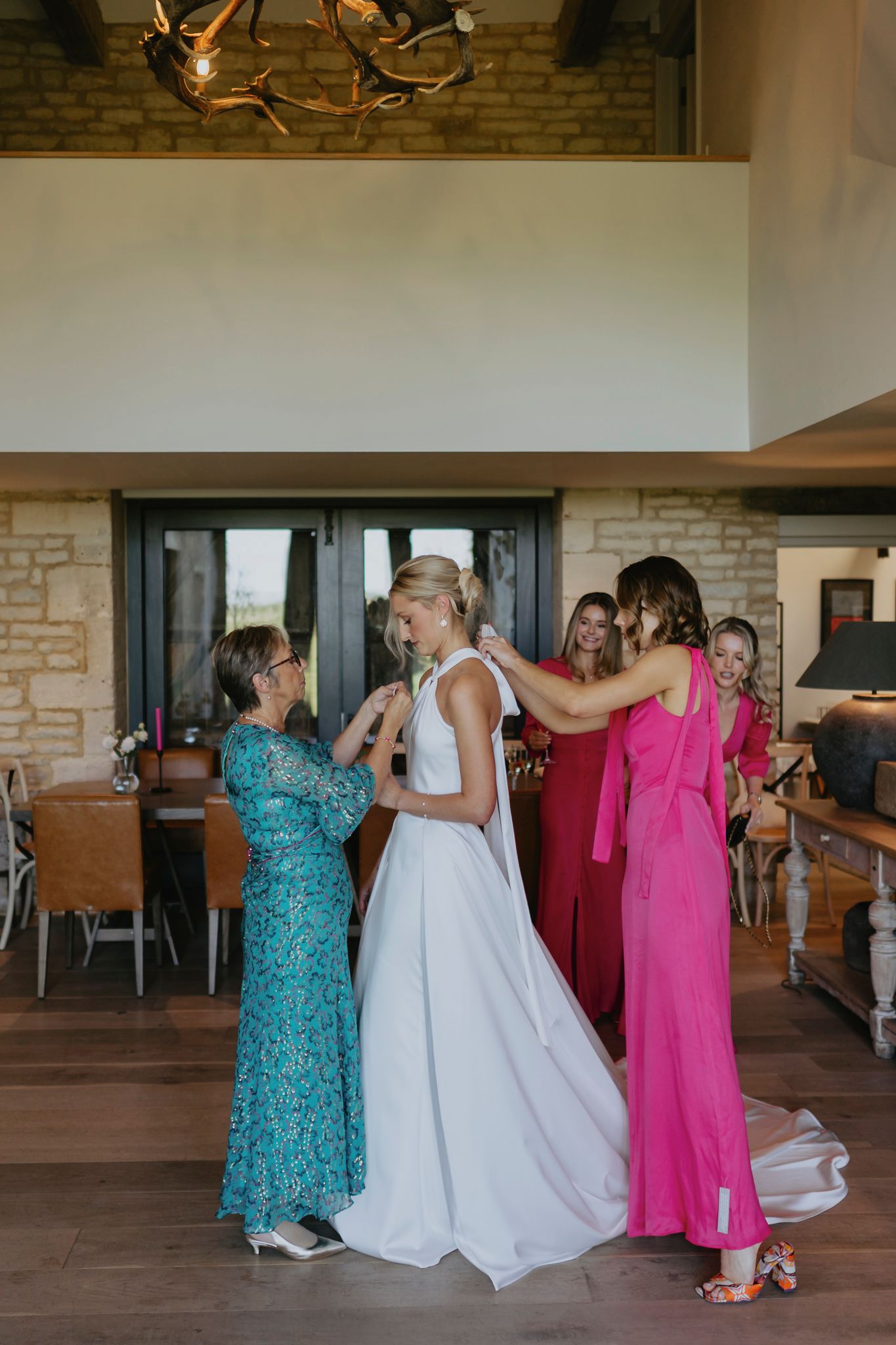 Wedding party helping with final adjustments of the bride's gown in an elegant stone-walled venue with rustic decor.