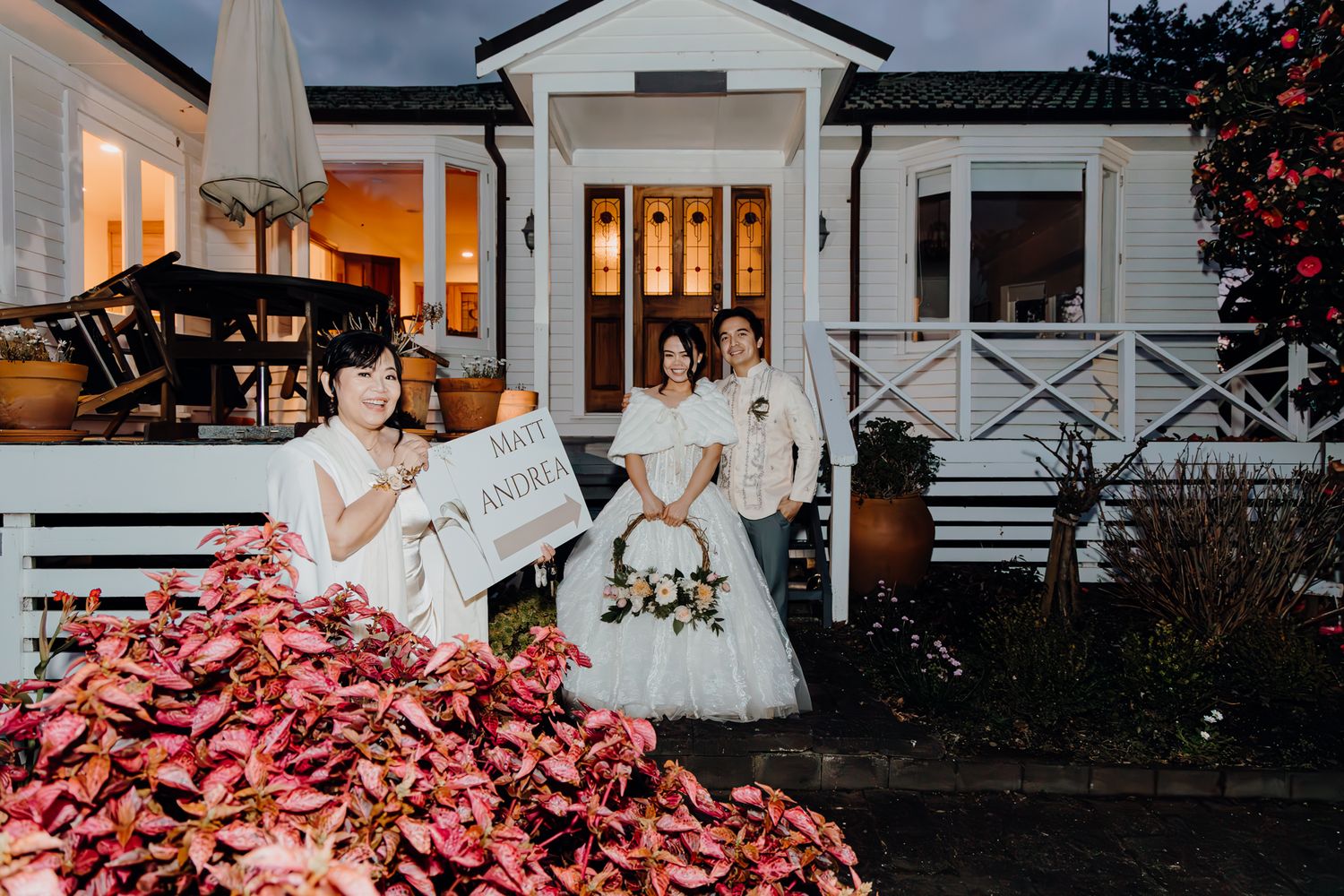 Evening portrait at a white house with warm glowing lights and pink flowering plants.