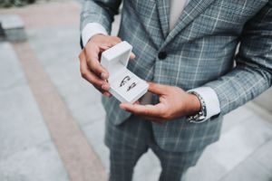 Groom in gray plaid suit holding open ring box.