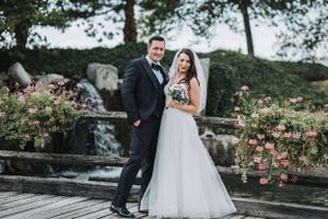 Elegant wedding portrait of couple on stone pathway surrounded by pink flowers.