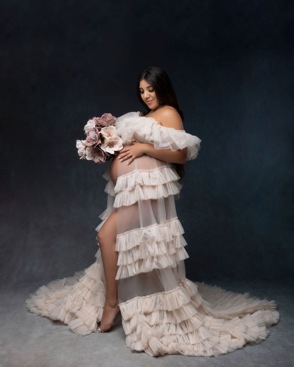 Ethereal maternity photoshoot with flowing white ruffled gown against dark backdrop creates dreamy atmosphere.