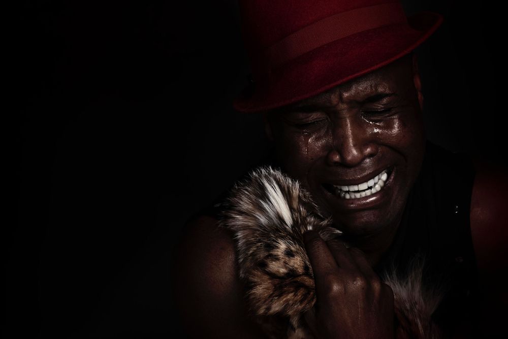 An emotional photo of Steven Haynes in a red hat holding a small furry dog in a dramatic low-light portrait.