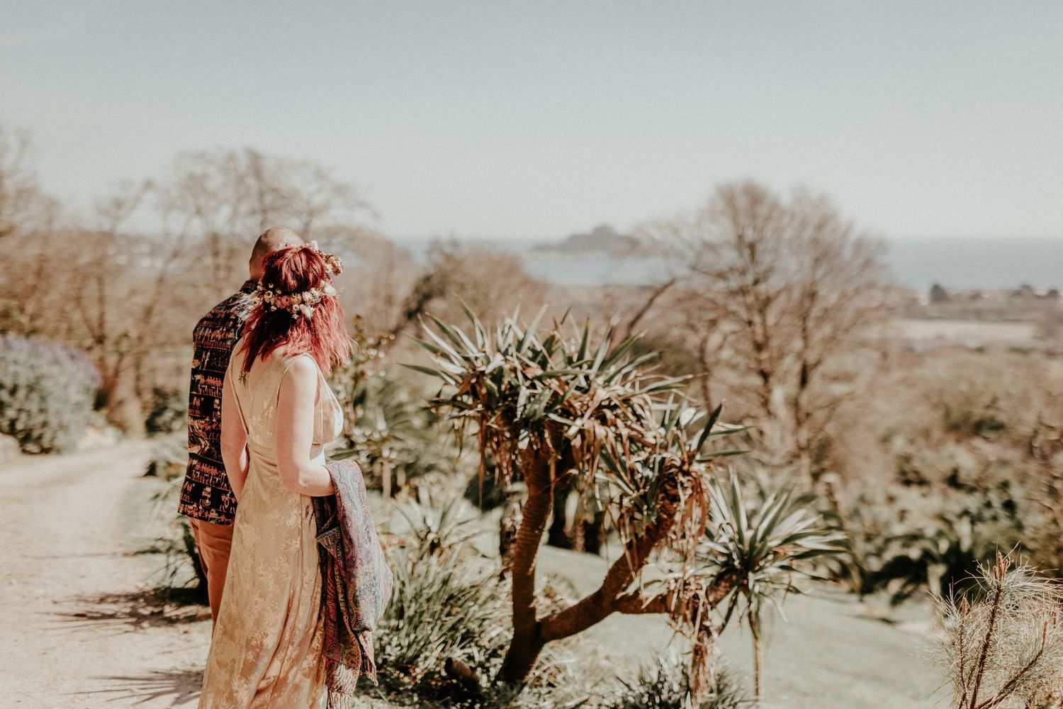 Couple in desert landscape embracing near blooming yucca plant with mountains visible in background.