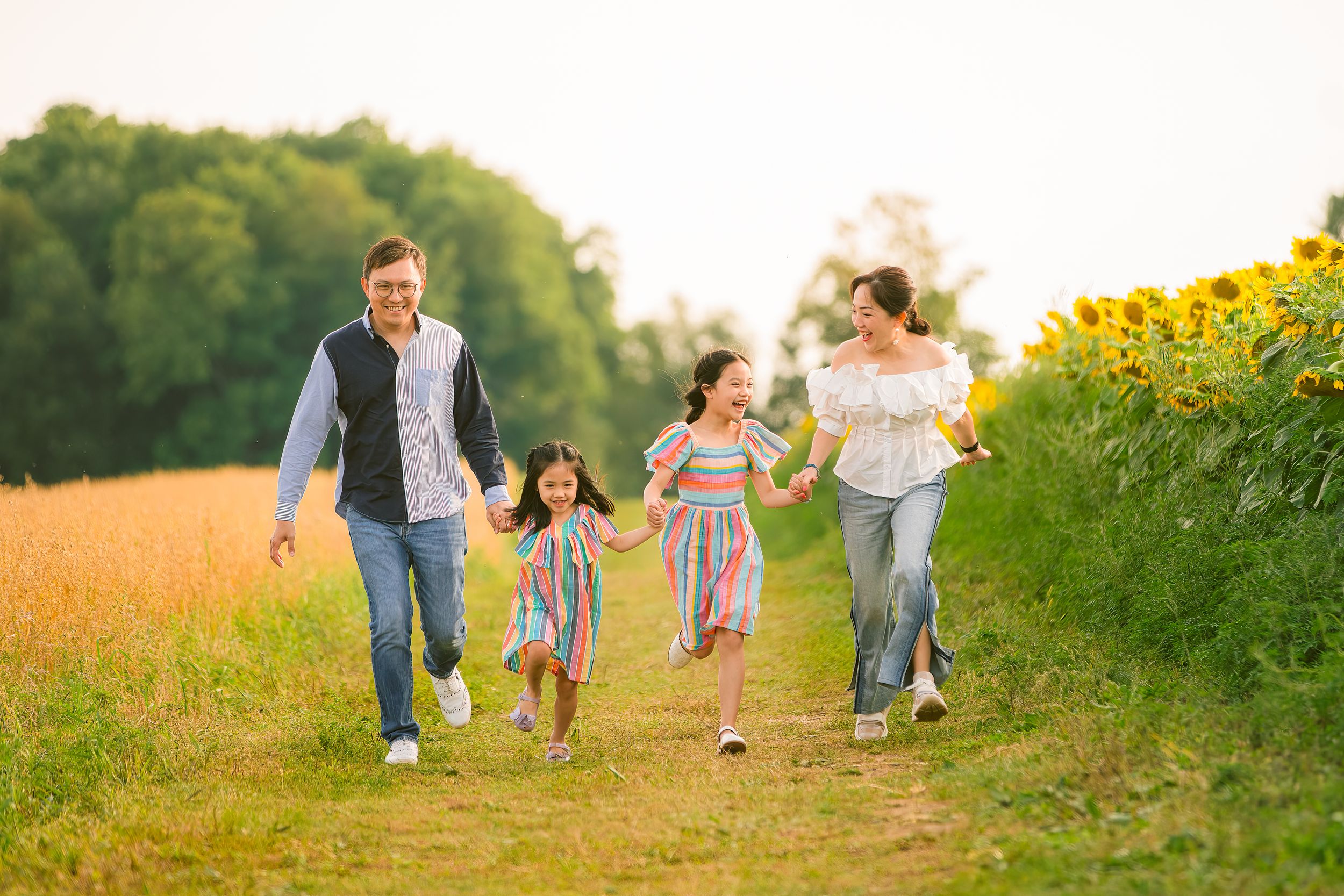 A family runs together joyfully through a golden field alongside blooming sunflowers at sunset.