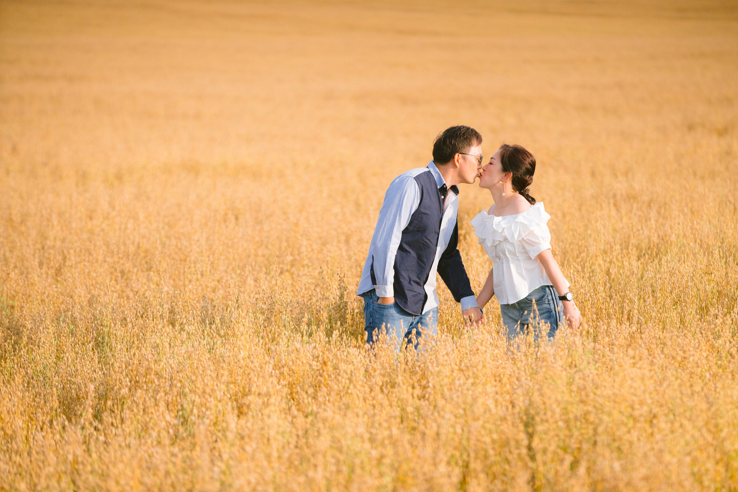 A couple shares a romantic moment in a sunny wheat field during golden hour.