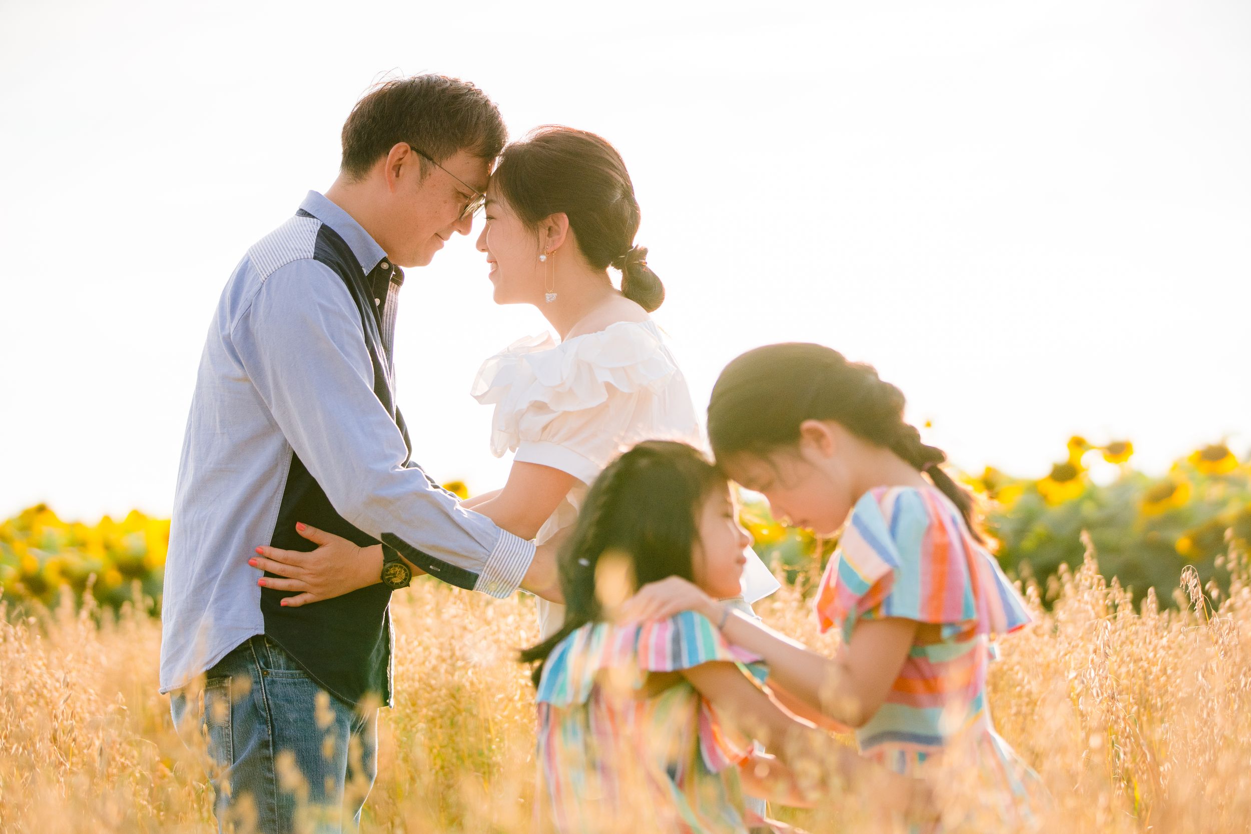 A family stands together in a golden wheat field at sunset with sunflowers in the background.