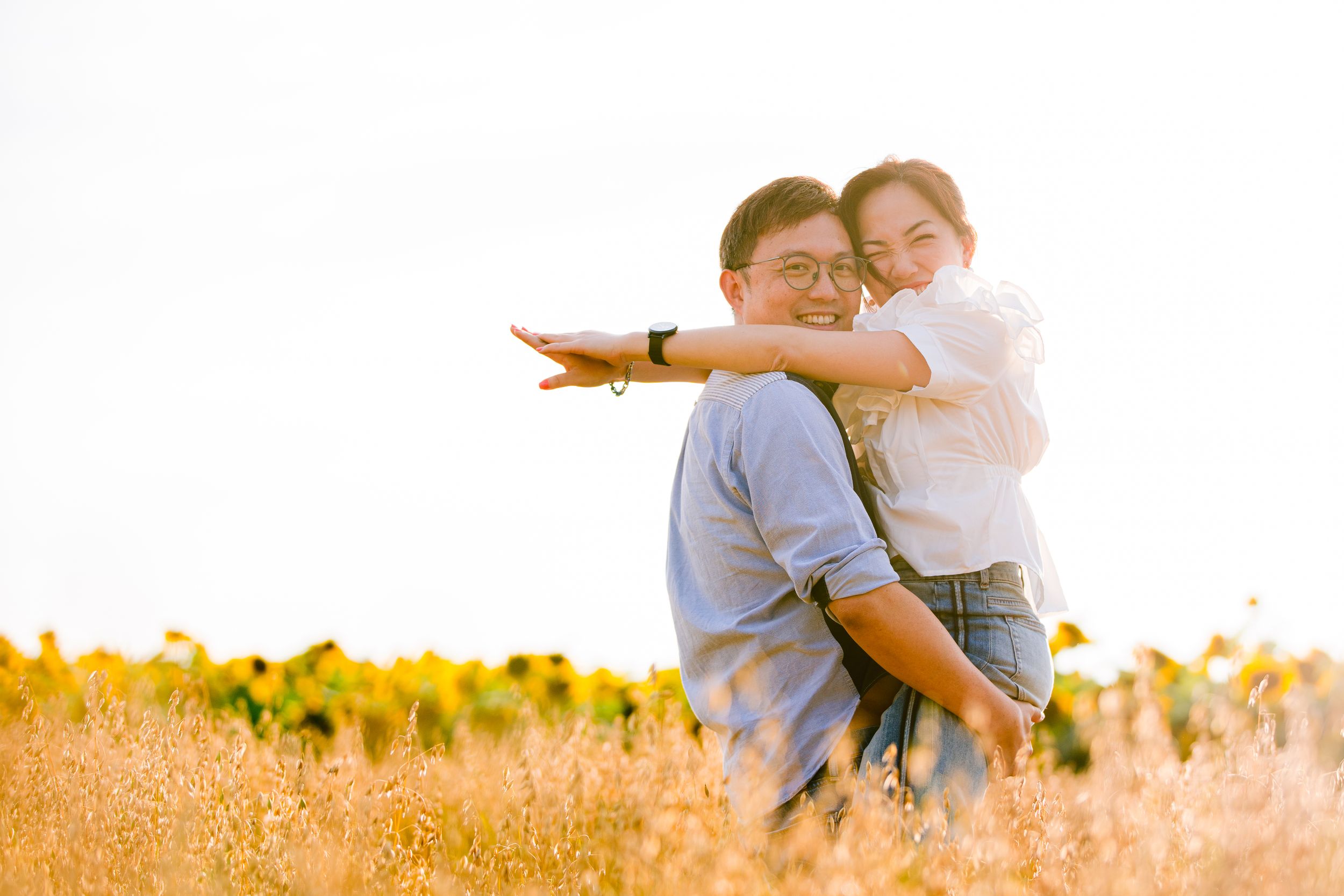 Two people sharing a joyful moment in a golden field with sunflowers in the background during sunset.