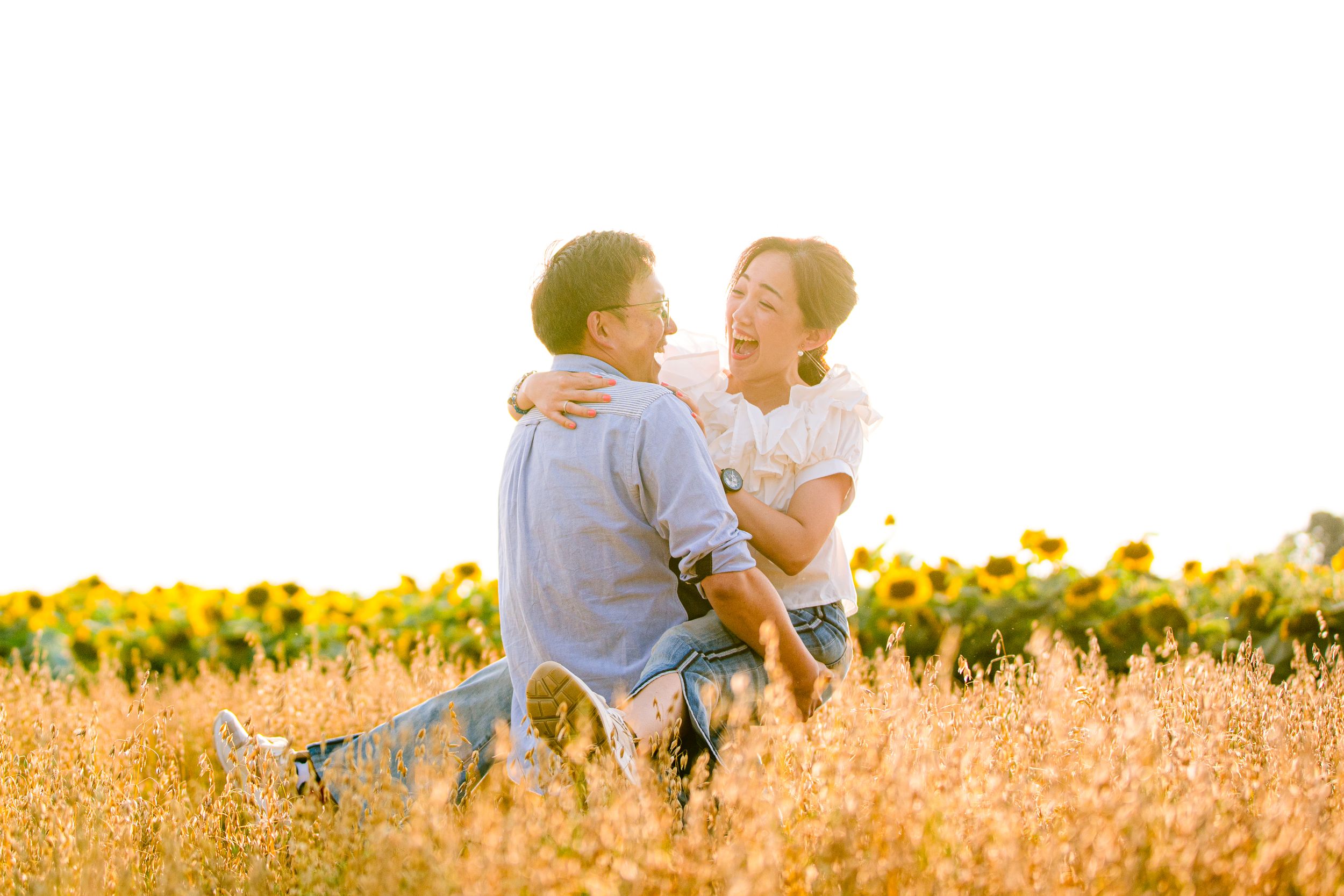 A loving couple embraces in a golden sunlit field of sunflowers during sunset.