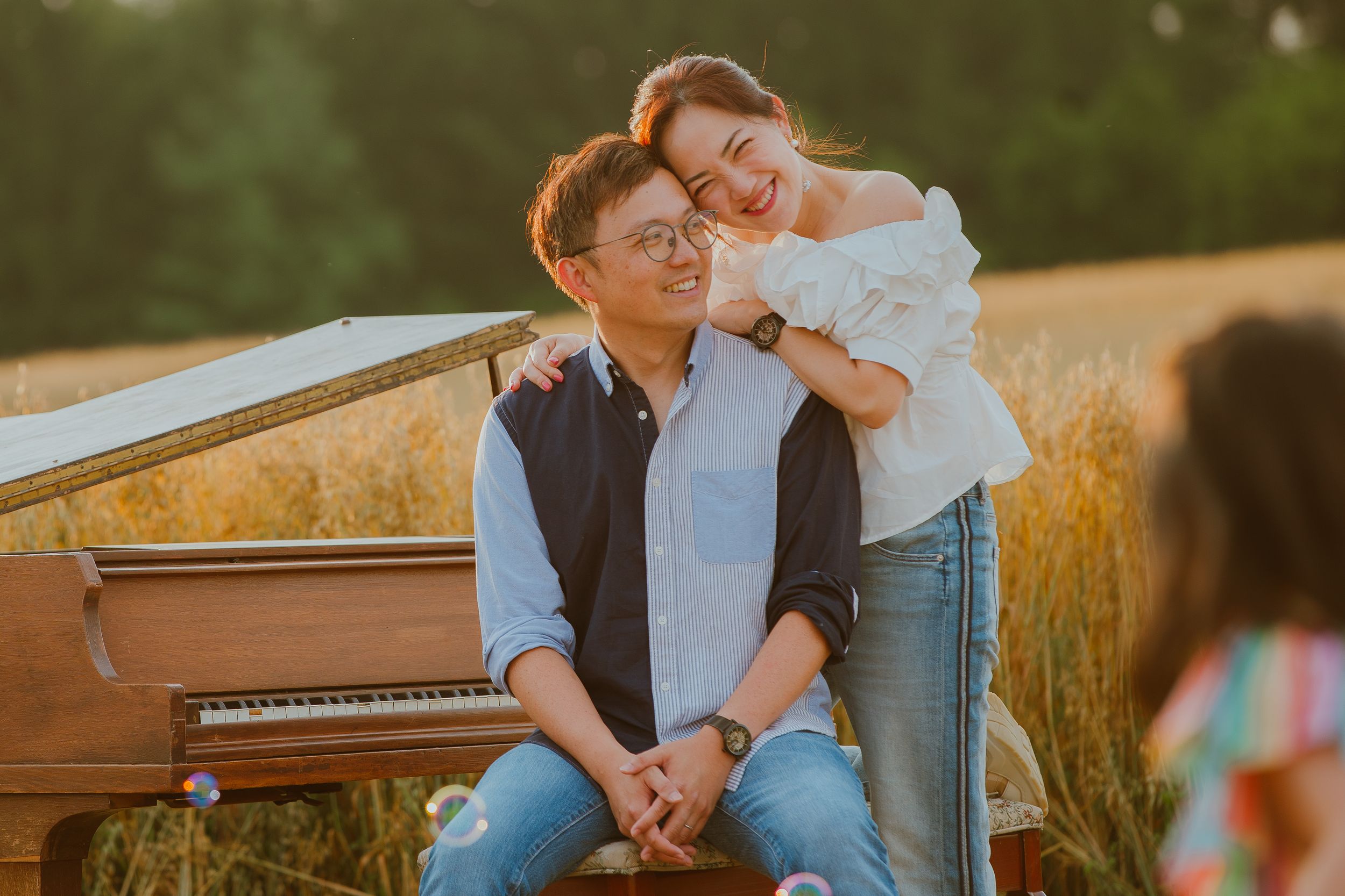 Two people share an intimate moment together at sunset with a piano in a golden wheat field.