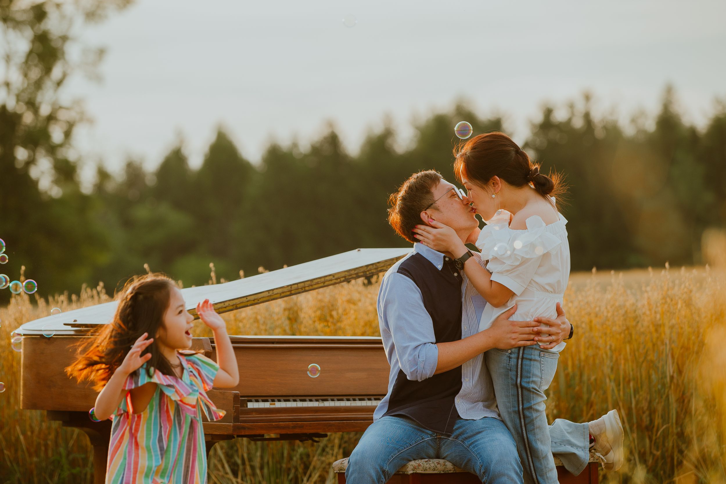 A family sits by an upright piano in a golden wheat field at sunset creating a warm and intimate outdoor moment.