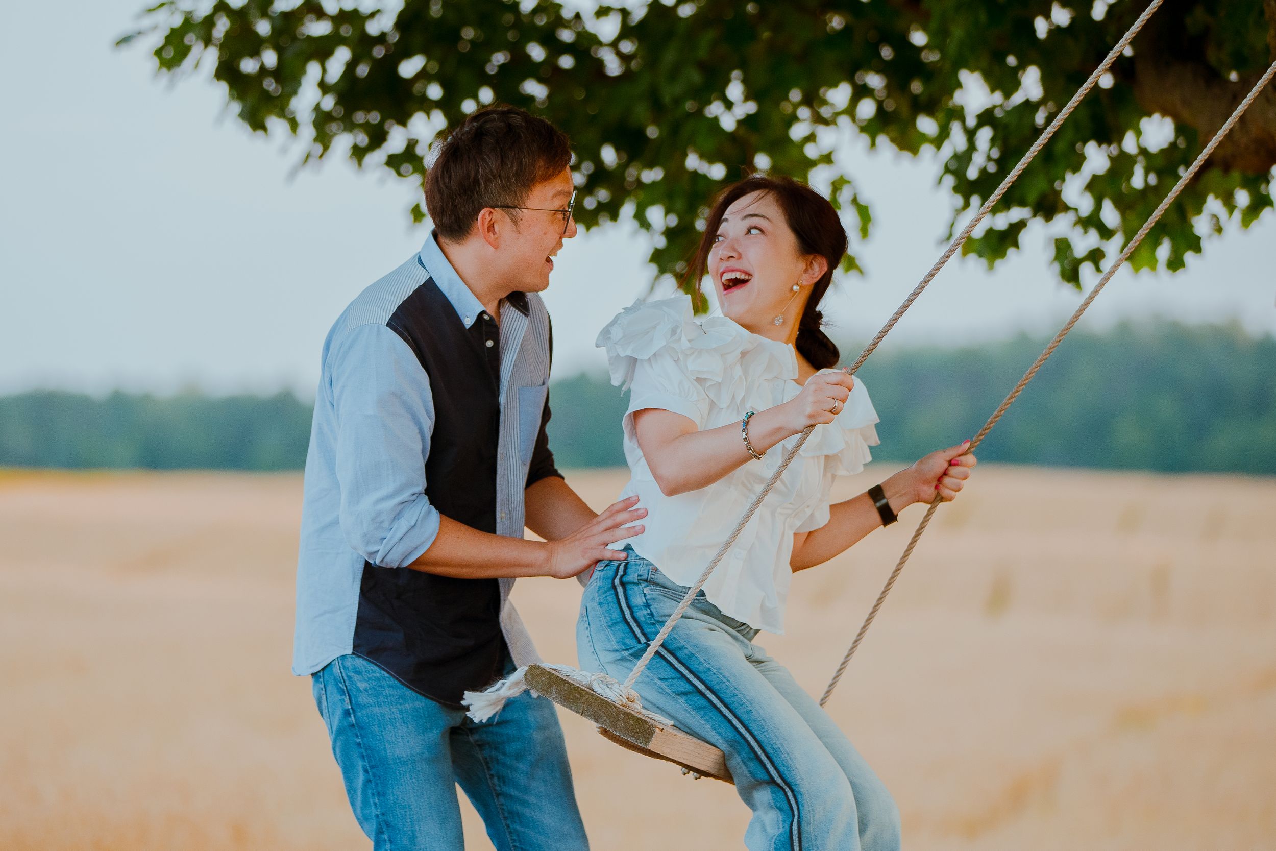A joyful couple laughing together while swinging outdoors at sunset in a natural setting.