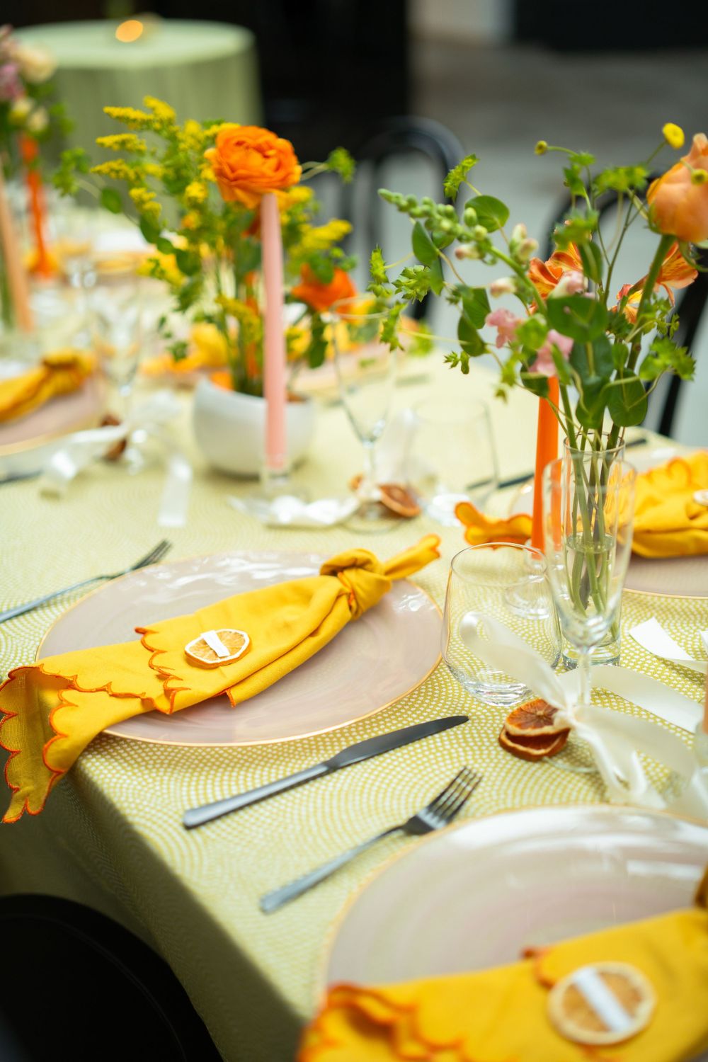 Elegant table setting with orange flowers and yellow napkins on a cream tablecloth for a formal dining event.
