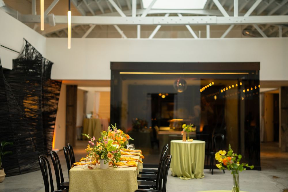 Modern event space with gold-draped tables and black chairs under exposed ceiling beams.