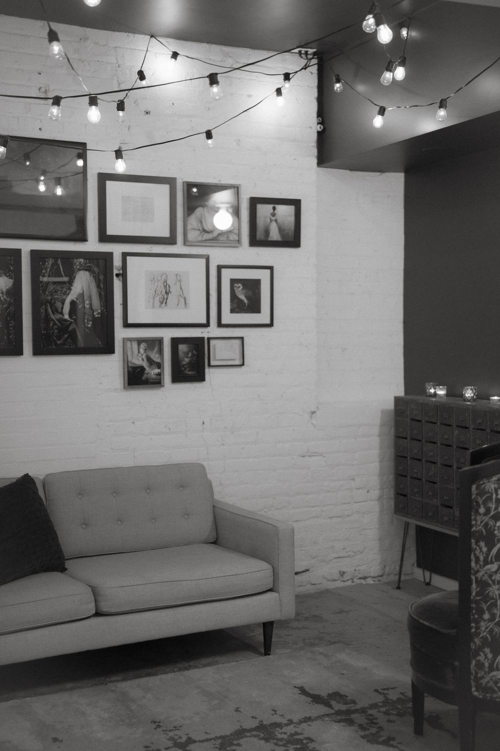 Cozy lounge area with string lights, gallery wall, and mid-century modern sofa.