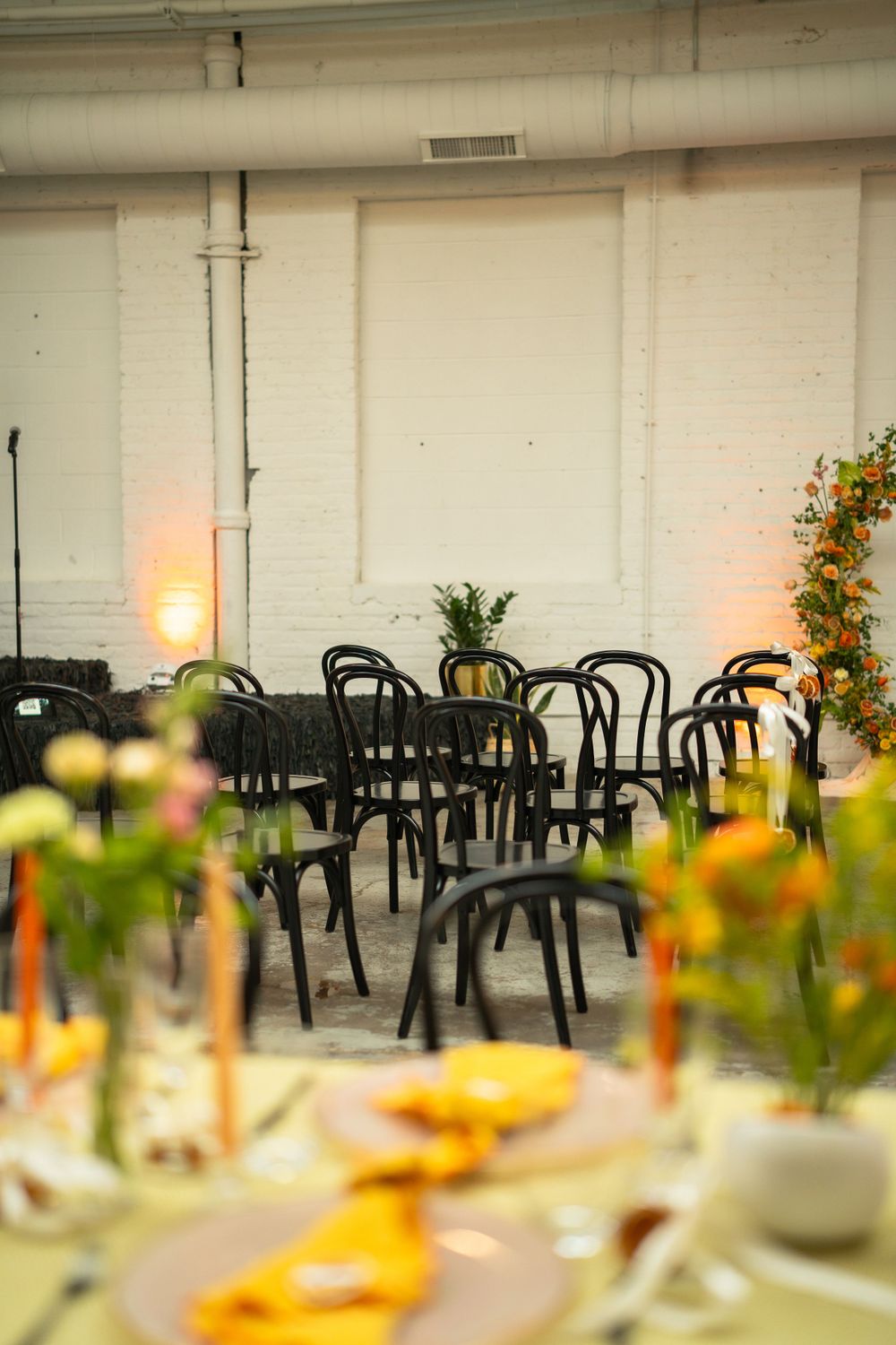 Wedding reception venue with black bentwood chairs and floral centerpieces in a white brick space.