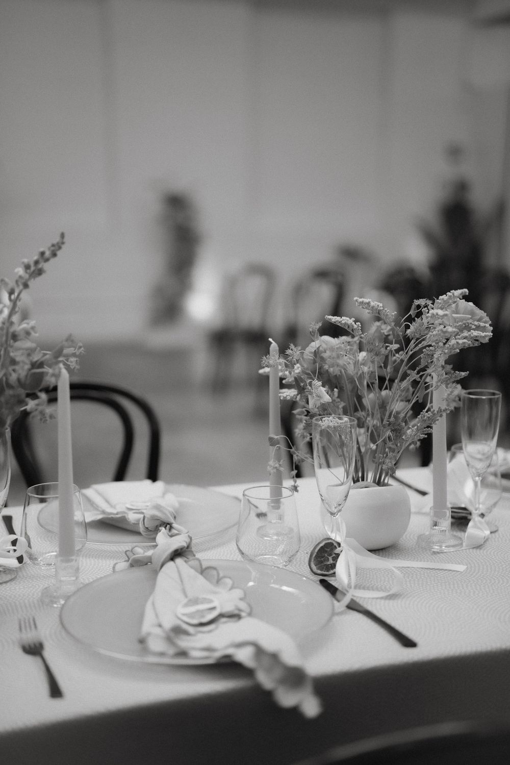 Elegant place setting with white flowers and candles on round dining table in black and white.