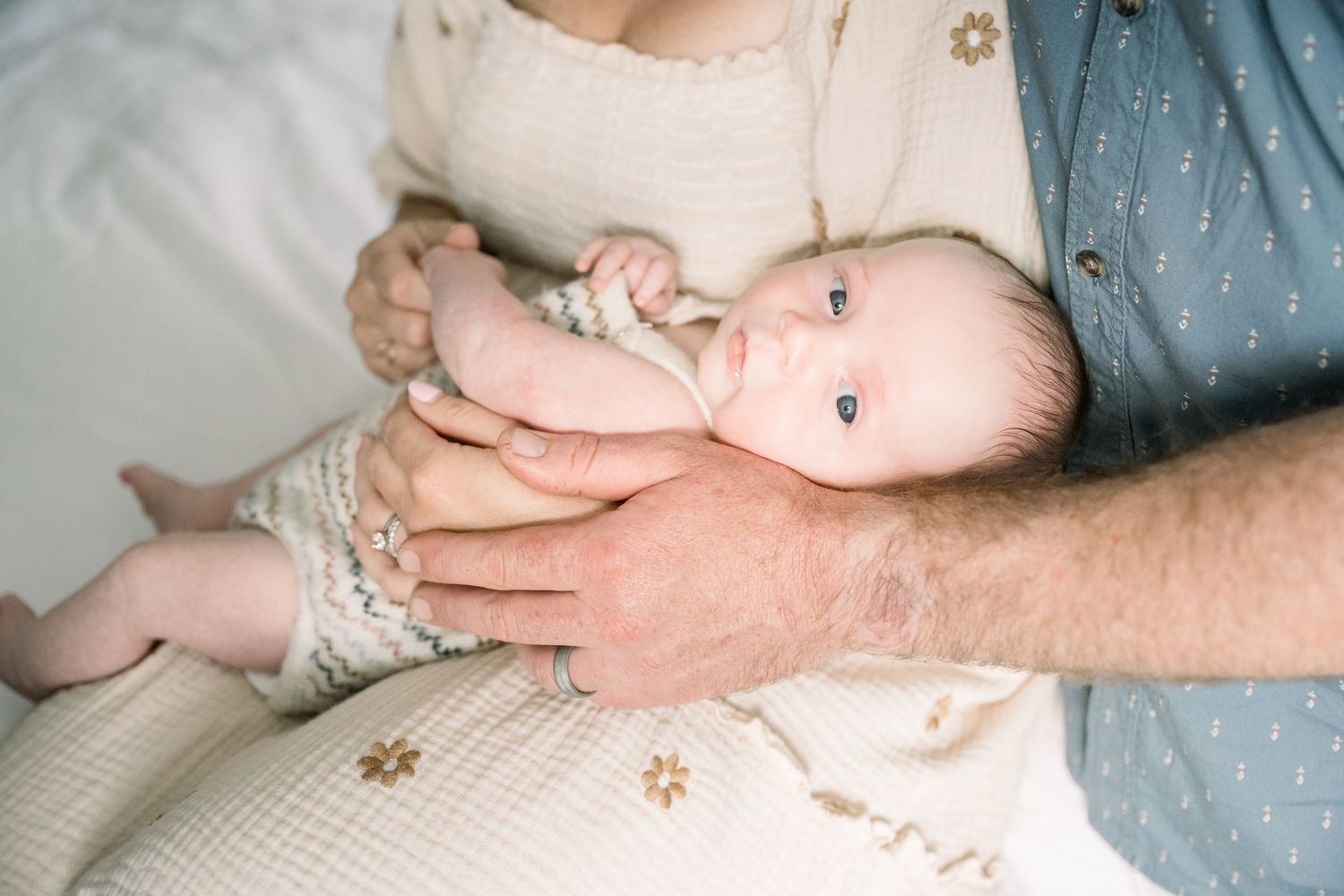 A tender family moment with new parents and their baby at home with a plant in the background.