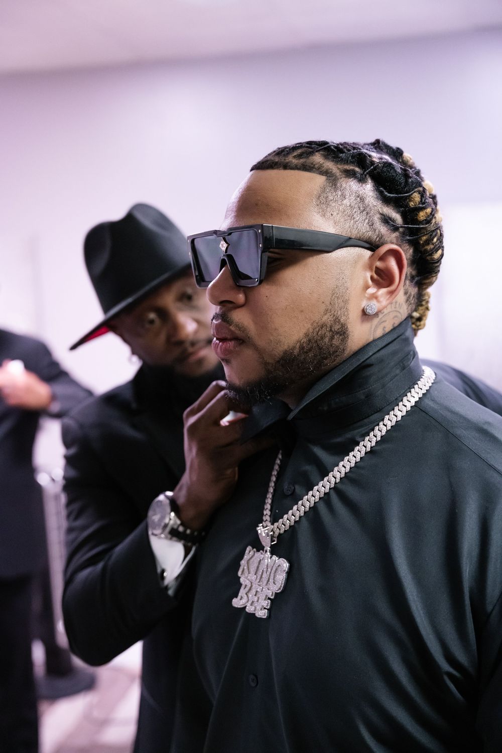 Two music artists in a candid backstage moment wearing black attire and stylish accessories.