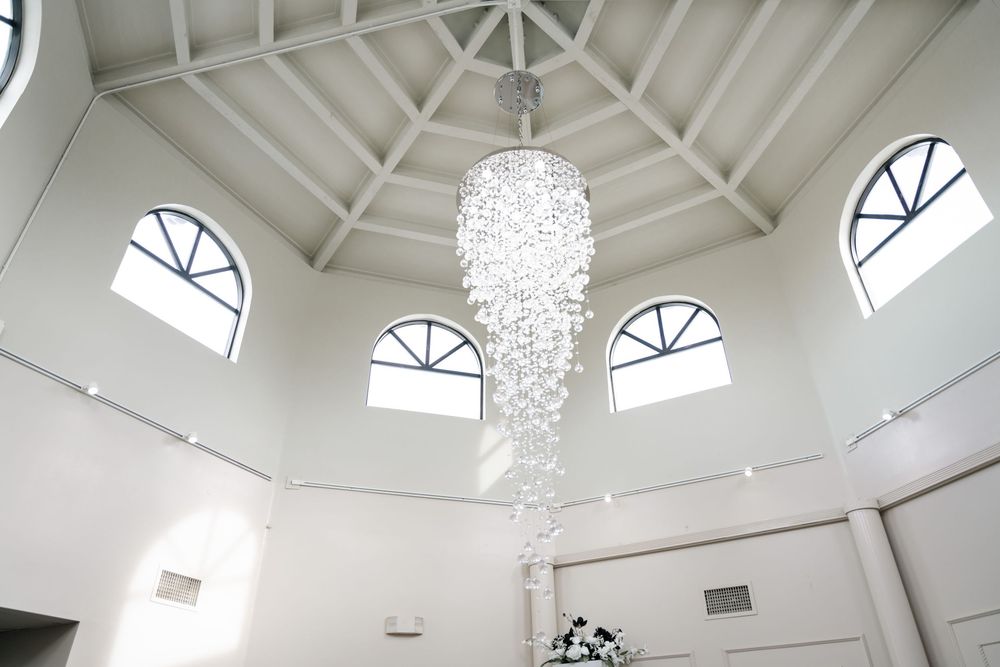 Elegant crystal chandelier hangs from white vaulted ceiling with arched windows in octagonal room.