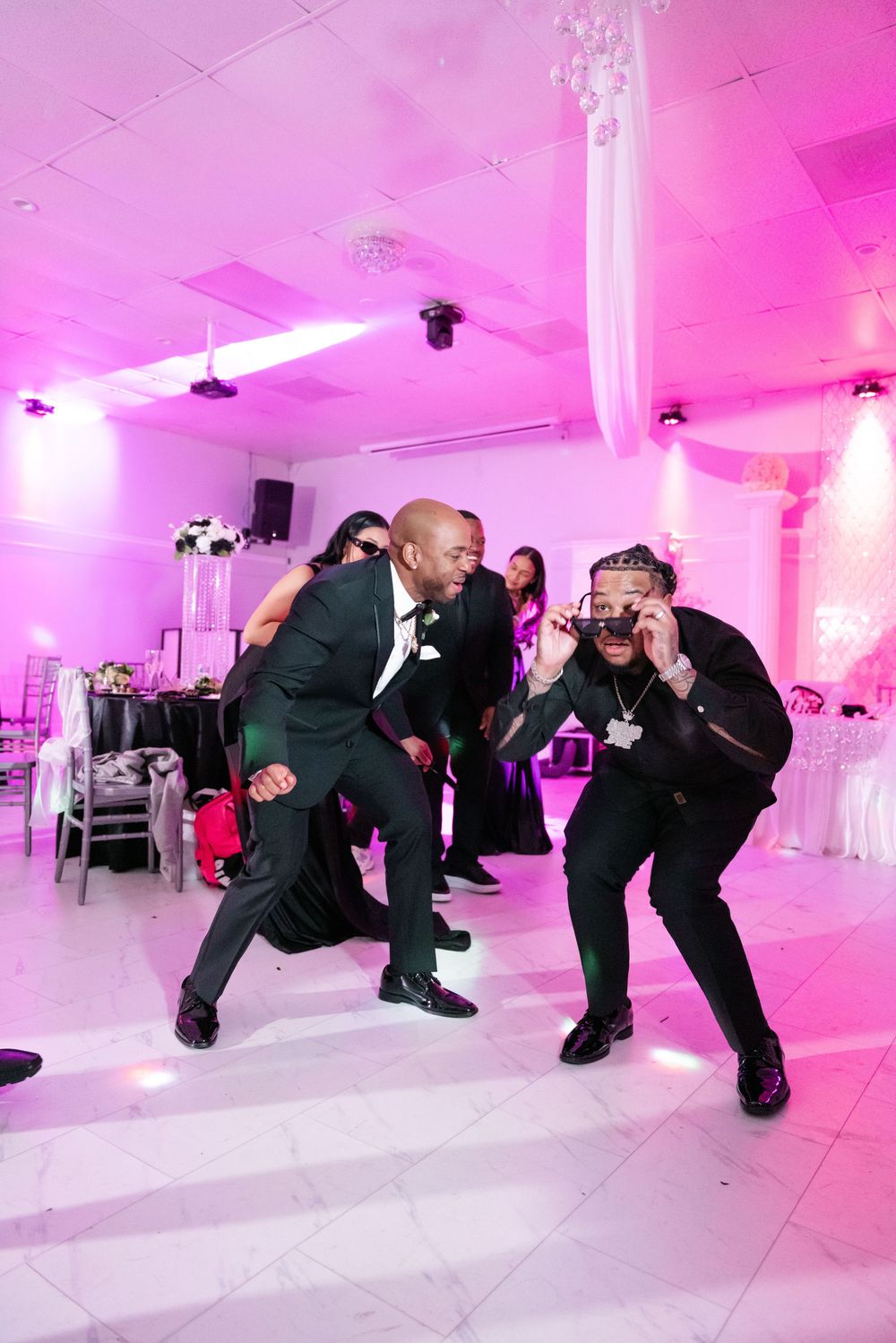 Wedding guests dancing and having fun on dance floor illuminated with pink lighting at a reception venue.