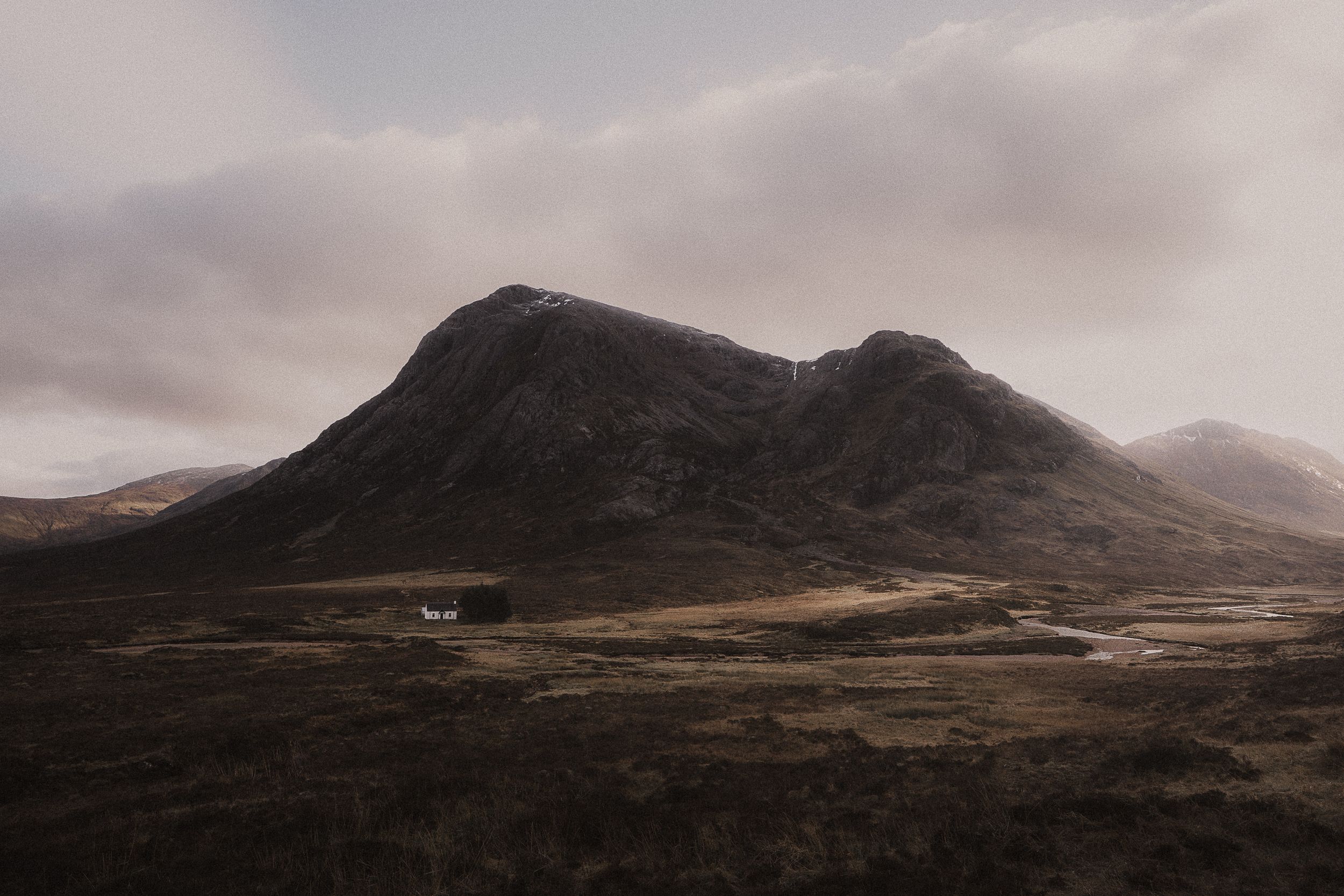 Moody mountain landscape in Scottish Highlands with dark peaks and cloudy skies over barren moorland.