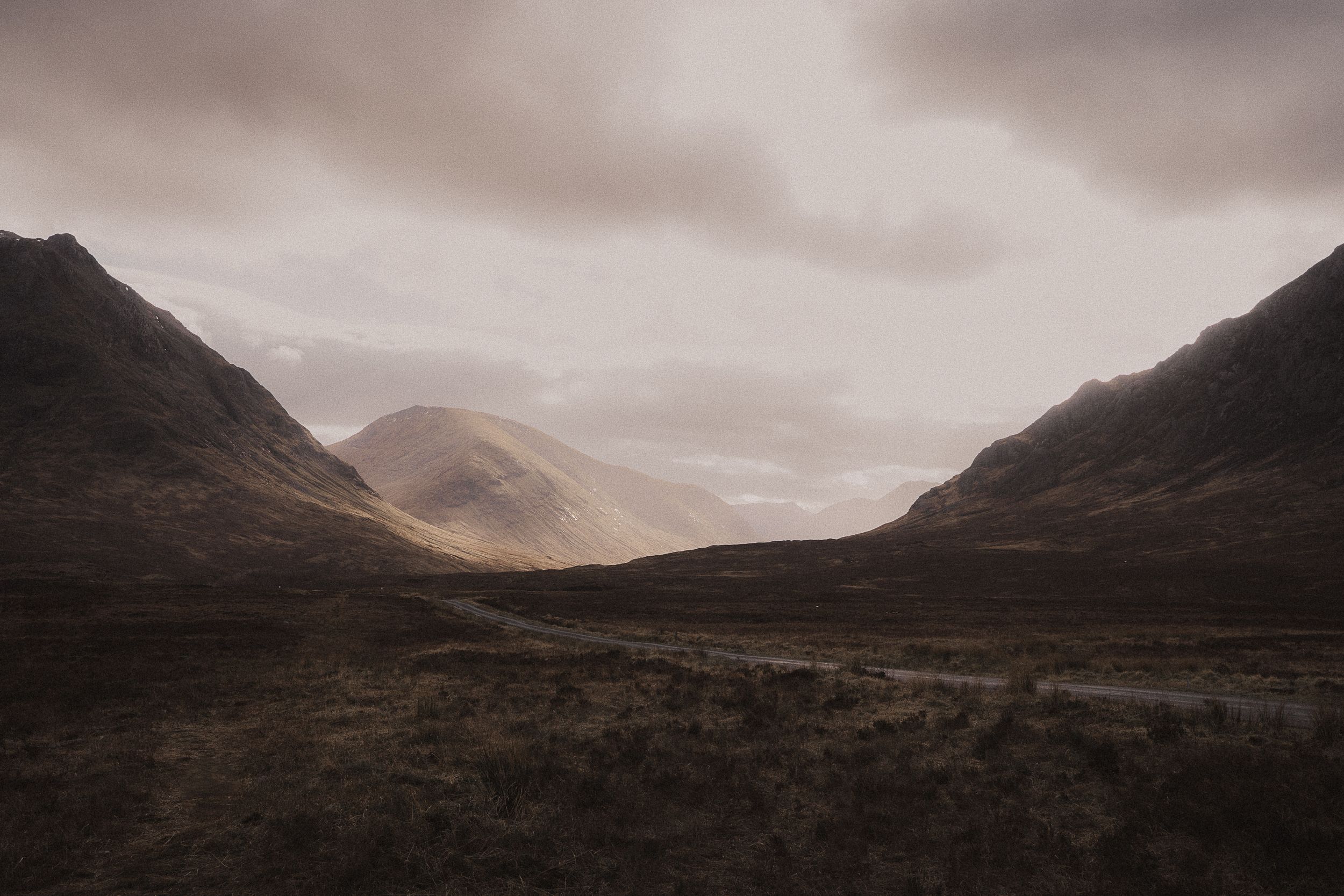 Dramatic panoramic view of rugged mountain peaks and valleys under moody overcast skies in Scotland's highlands.
